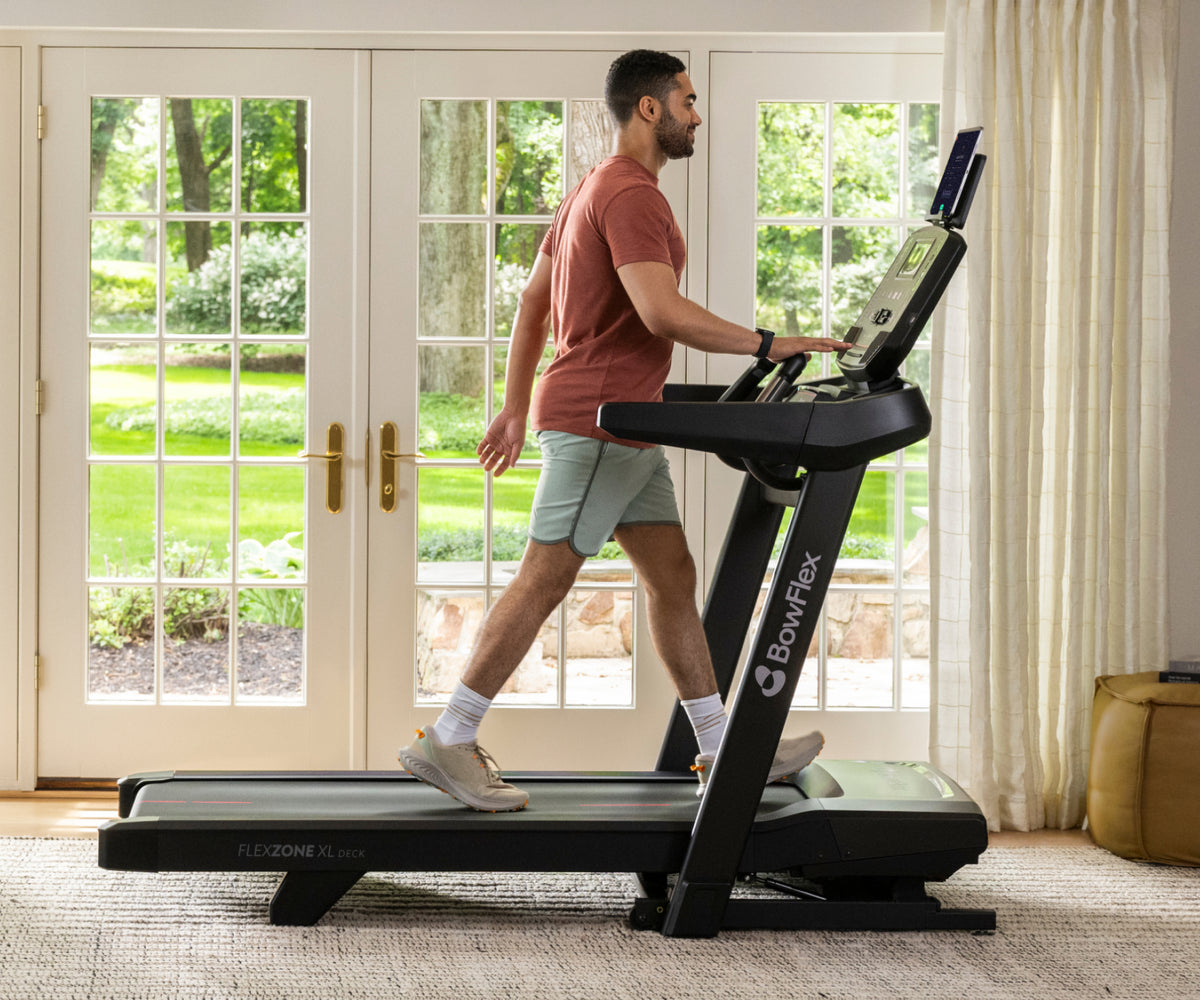 A man running on the BowFlex T9 Treadmill inside a bright, modern room with large white French doors and a light-colored rug.