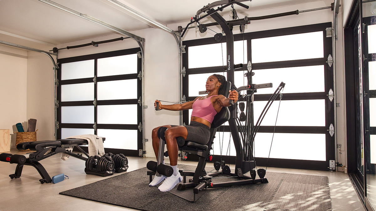 Woman using the cable pulley system during a seated workout on the BowFlex Xtreme 2 SE in a home gym.