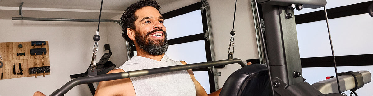 A man in a home gym wearing a white tank top working out on the BowFlex Xtreme 2 SE Home Gym.
