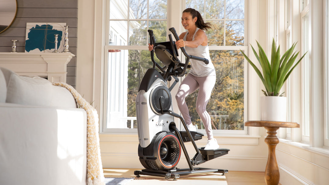 Woman exercising on a BowFlex Max Trainer M6 in a home setting.