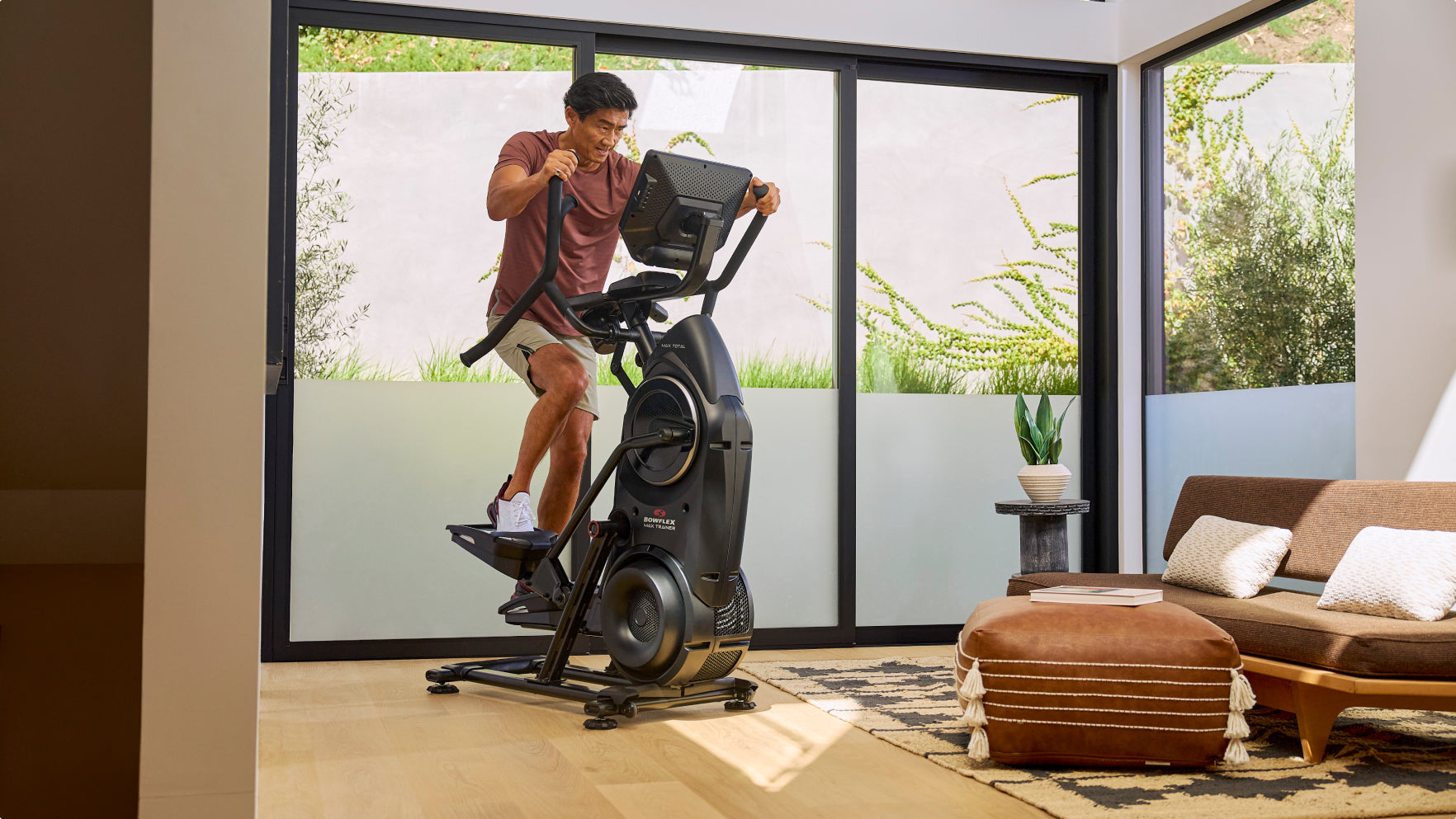 A man riding a BowFlex Max Total 16 in a modern living room.