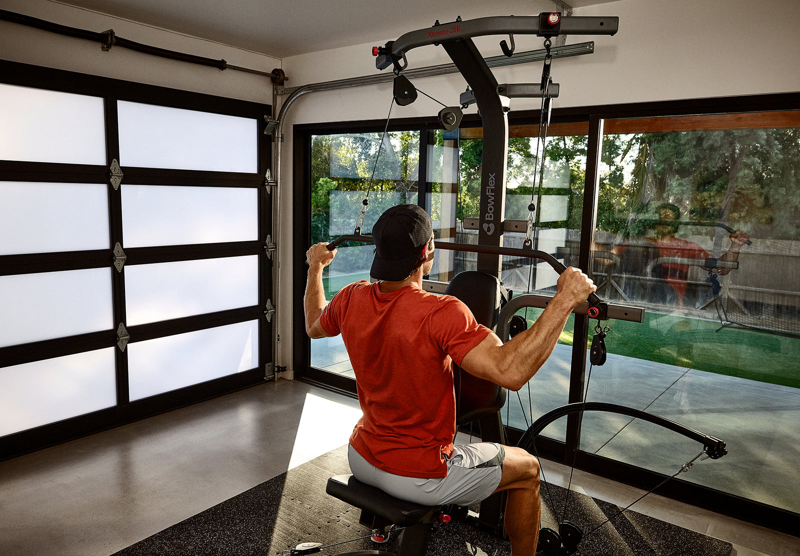 A man seated on and facing the BowFlex Xtreme 2 SE using its angled lat bar to workout in a home gym.