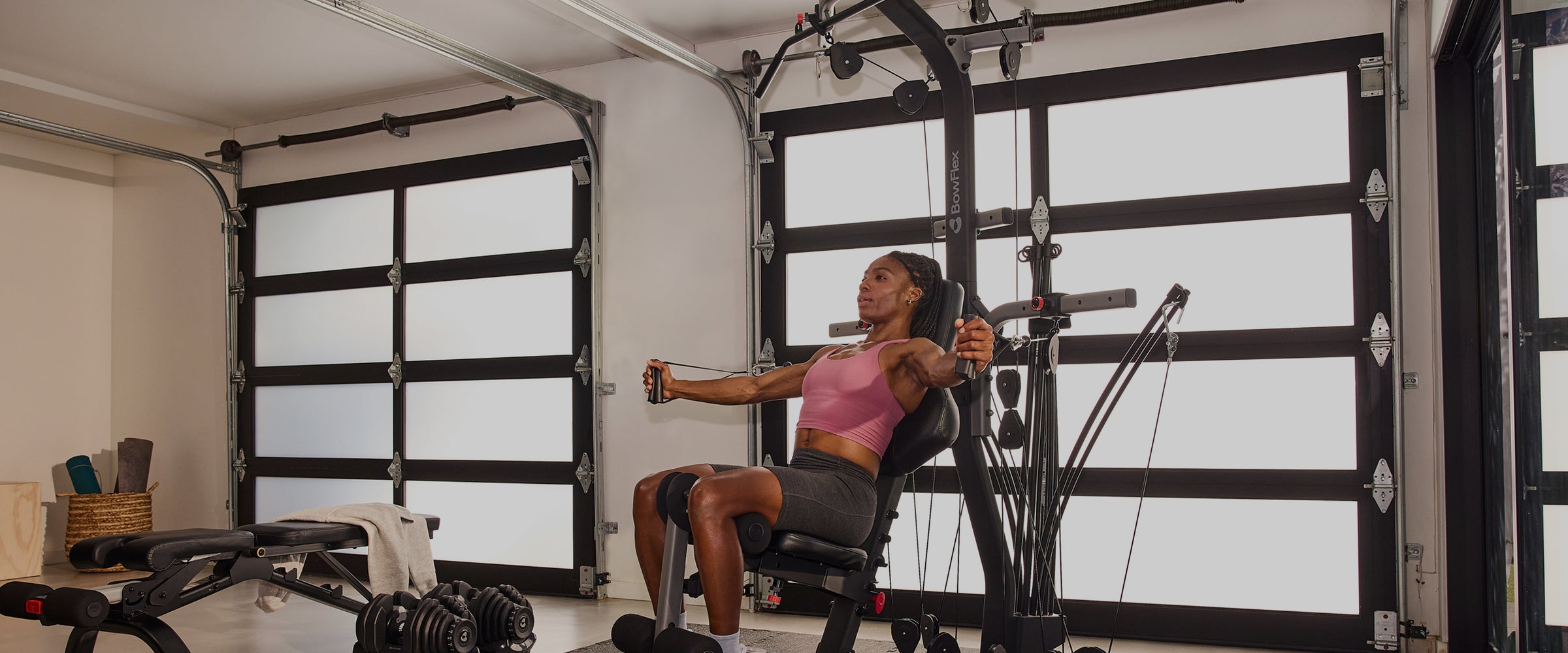 A woman exercises on the BowFlex Xtreme 2 SE Home Gym inside a modern garage with white garage door panels.