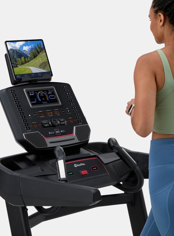 Woman looking at JRNY app screen on a tablet placed on the BowFlex T9 Treadmill media shelf.