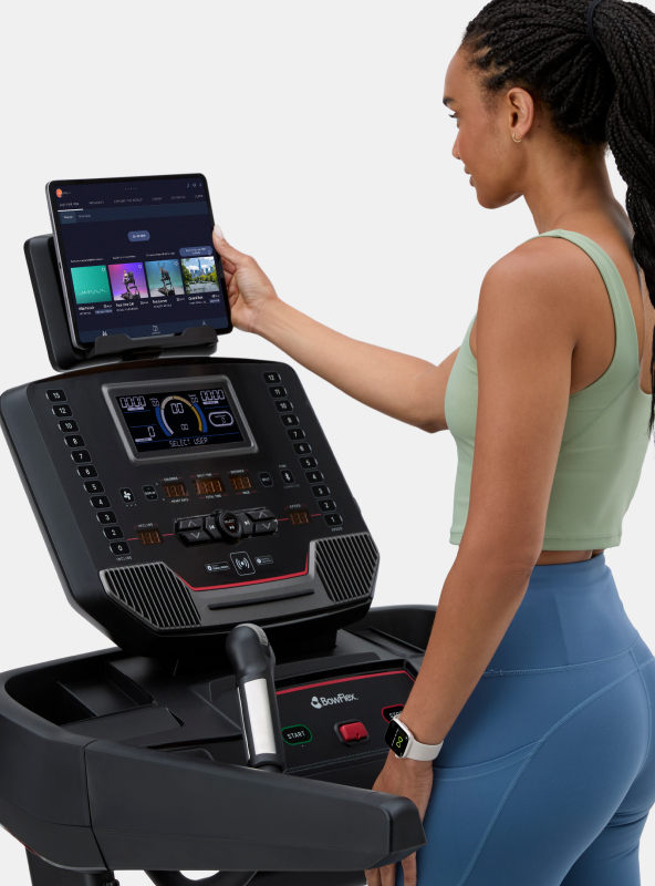 Woman interacting with tablet placed on the BowFlex T9 Treadmill media shelf.