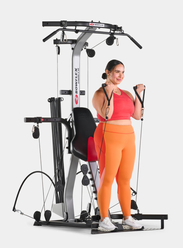 Woman standing in front of the BowFlex Xtreme 2 SE using its hand grips.