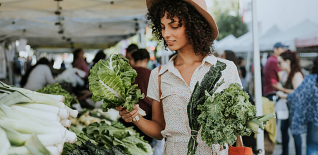 A woman holding leafy greens at an outdoor market.