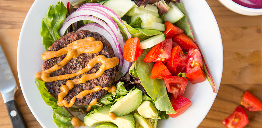 Close up image of burger salad. Hamburger patty on top of vegetables.
