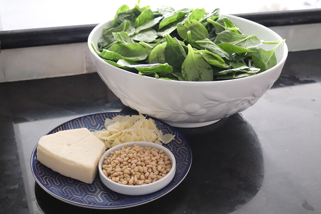 spinash in a bowl next to parmesan cheese and pine nuts.