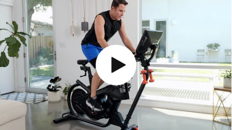 A woman is riding an exercise bike with a play button in the corner