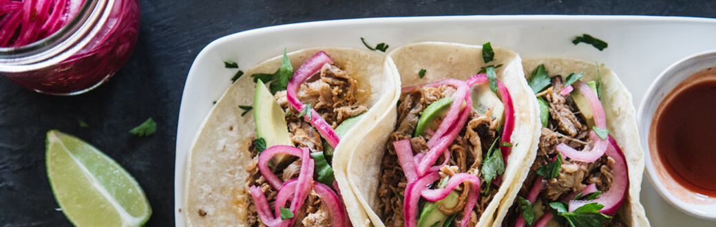 Three pulled pork tacos on a plate.