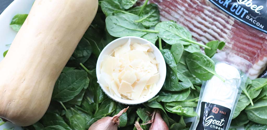 butternut squash sitting on spinach leaves plus bacon and shaved parmesan