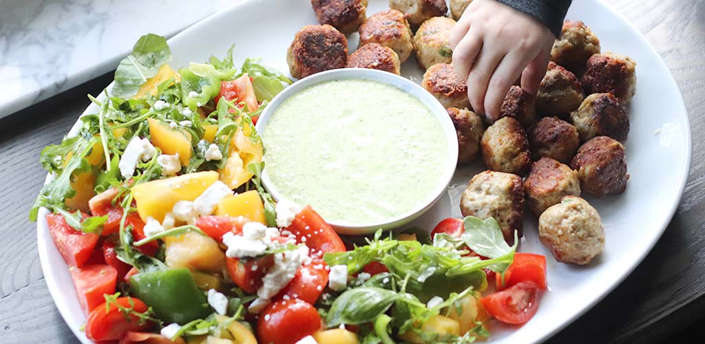 Greek chicken meatballs on a plate with greek salad and dip.