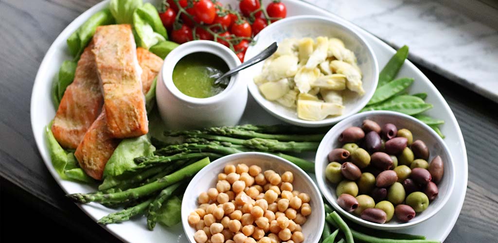 Salmon, pesto, tomatoes, artichoke, olives, chickpeas, and asparagus on a serving dish.