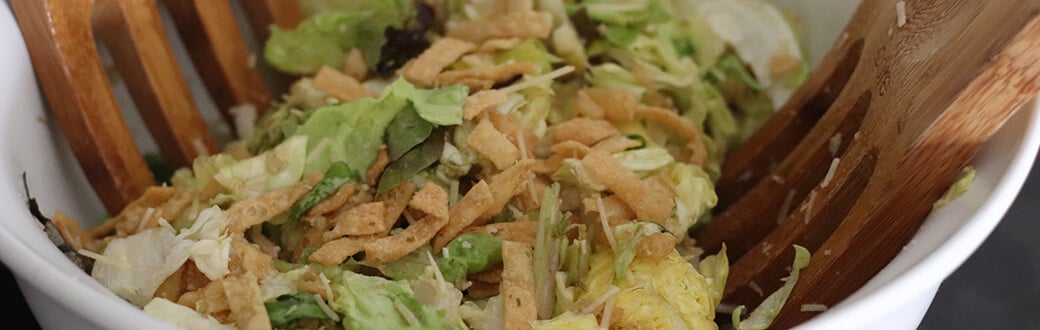 A bowl of ceasar salad with wooden serving utensils.