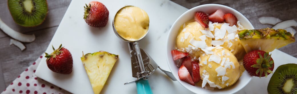 A bowl of mango ice cream with strawberries and coconut shavings.