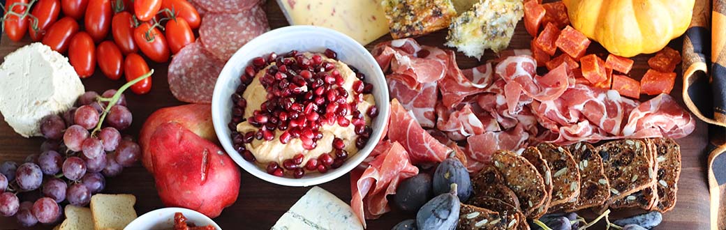 Close-up view of a meat, veggie, and cheese platter featuring pumpkin hummus