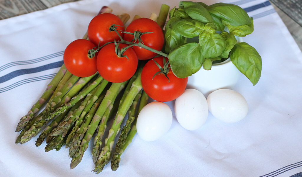 asparagus, tomatoes, basil, and eggs on a counter.