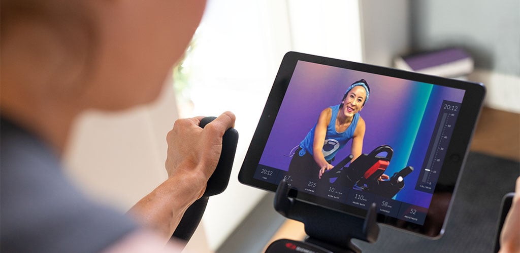 A woman riding an exercise bike while watching instructional JRNY video.