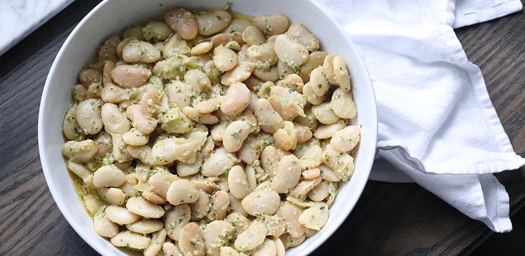 Butter beans in pesto oil in a serving dish.