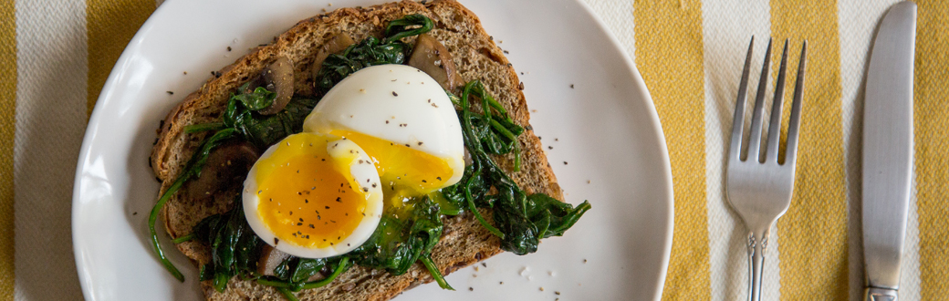 A halved soft boiled egg on cooked spinach and toast.