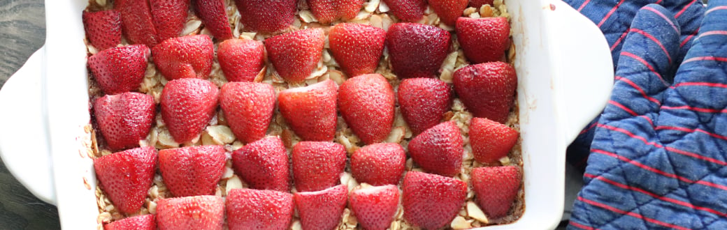 Baked strawberry oatmeal in a casserole pan with oven gloves