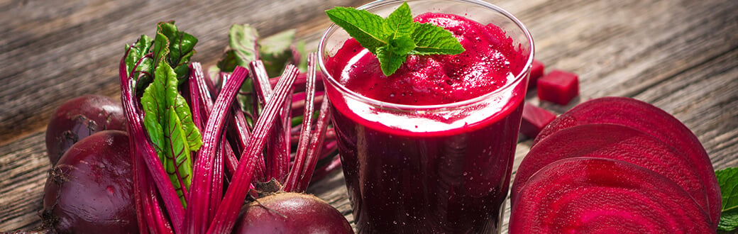 A glass of beetroot juice surrounded by beets.