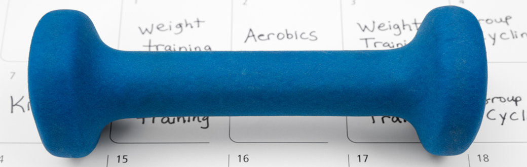 A dumbbell sitting on a workout calendar.