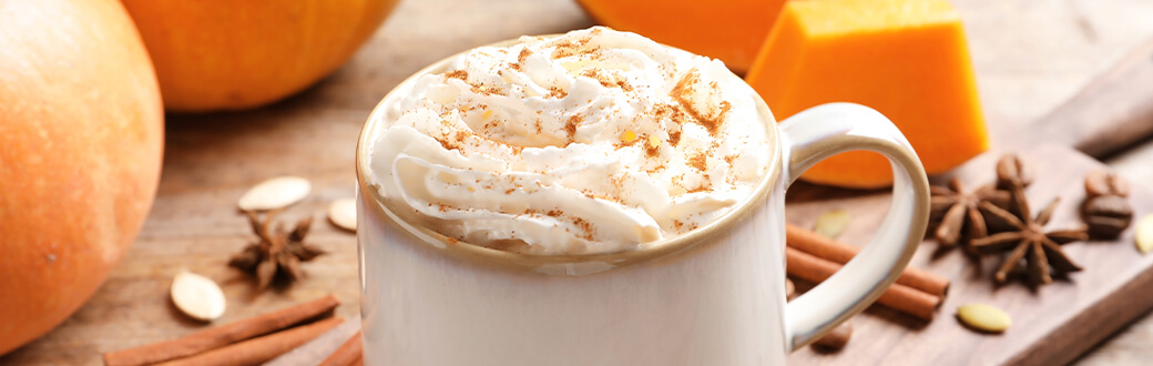 A pumpkin spice latte with whipped cream on a wooden table.