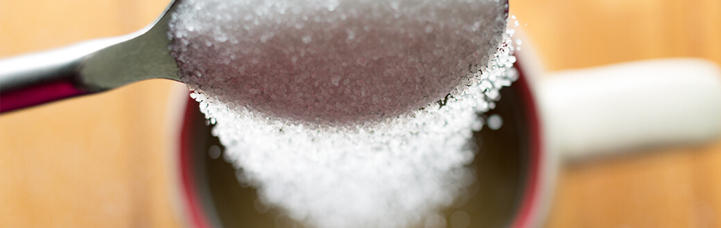 A spoonful of sugar being poured into a cup.