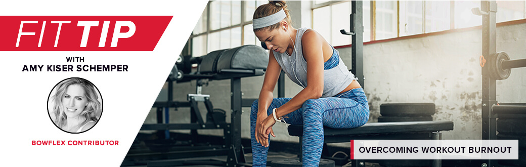 A fit woman in a gym sitting on a bench looking tired.