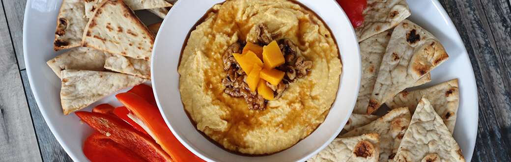 A bowl of butternut squash hummus surrounded by sliced pita.