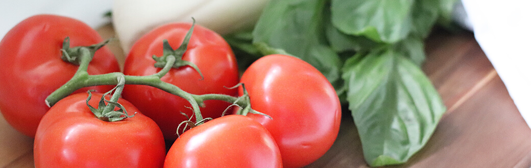 Tomatoes on the vine and basil on a wood cutting board.