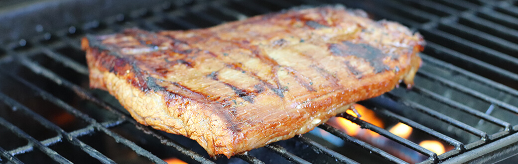 A cut of flank steak cooking on a grill.