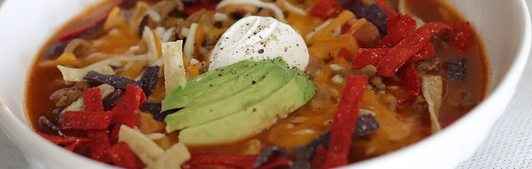 A bowl of ground turkey chili topped with sour cream, avocado, and tortilla strips.