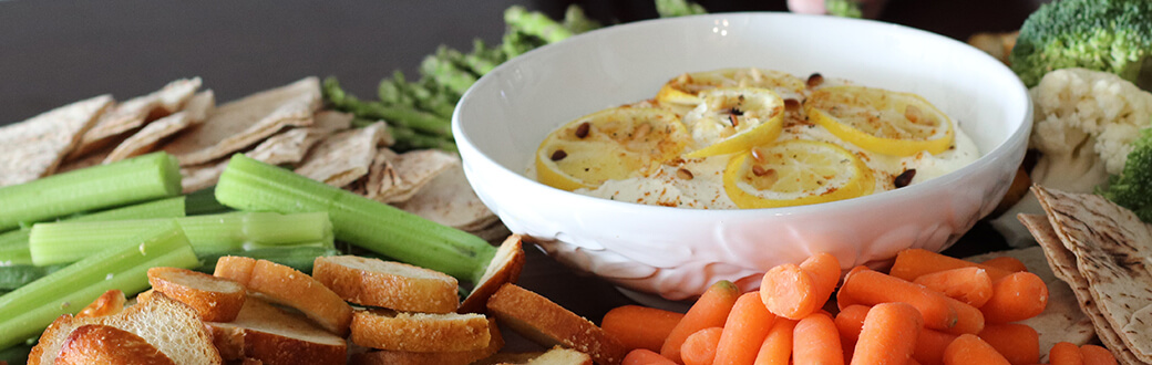 Lemon feta dip in a bowl surrounded by veggies and pita bread.