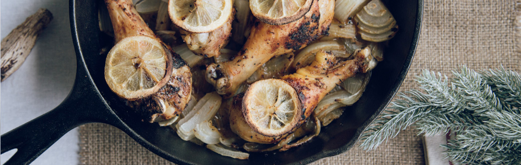 Roasted chicken legs topped with lemon slices in a cast iron skillet