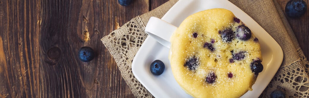 A mug muffin with blueberries sitting on a table.