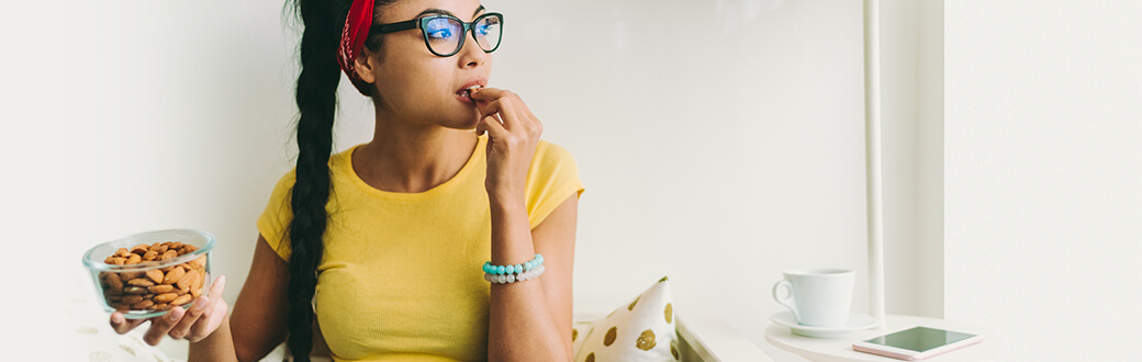 A woman eating from a small bowl of almonds.