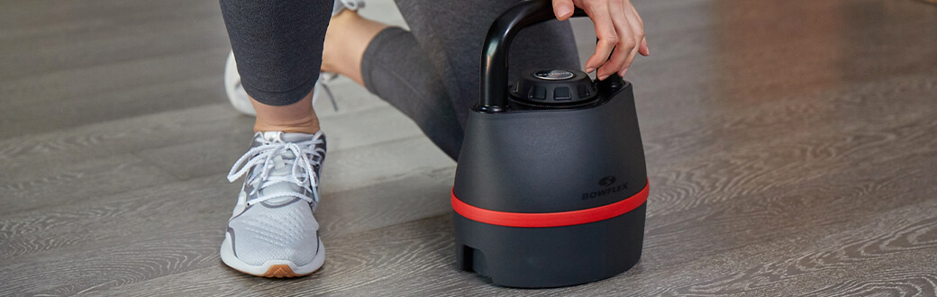 A person kneeling next to a bowflex selecttech 840 adjustable kettlebell