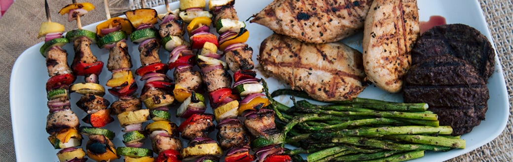 Barbecued foods including asparagus, hamburger patties, chicken and kebab skewers