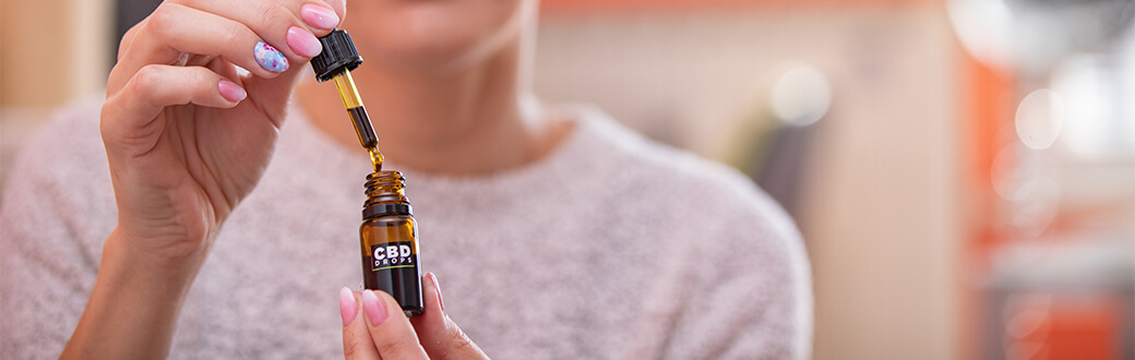 A person using a glass medicine dropper on a CBD oil container.