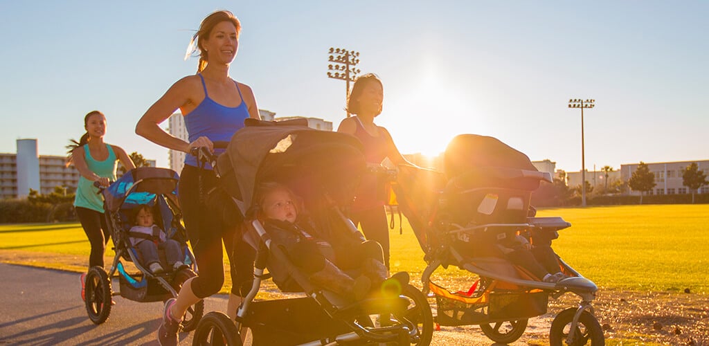 3 women running outside while pushing strollers.