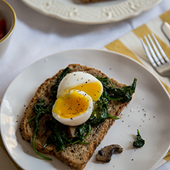 Close up image of a soft boiled egg on top of cooked spinach on toast.