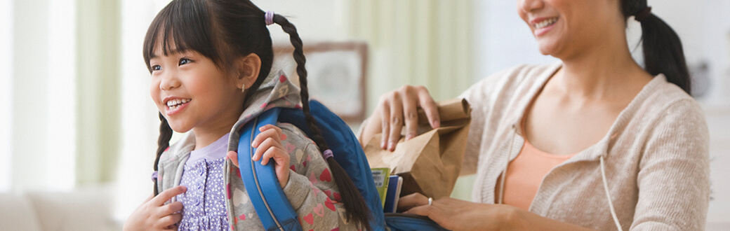 A mom putting lunch into her daughter's backpack.