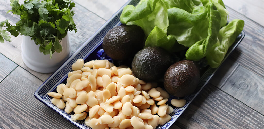 Cilantro, white beans, avocado, and lettuce on a counter.