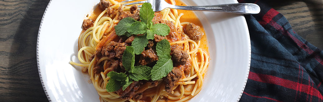 Plate of lamb Bolognese served on bucatini pasta.