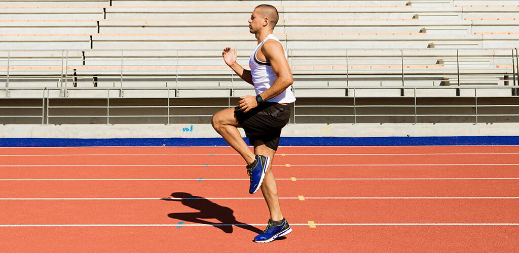 A man on a track performing high knees.