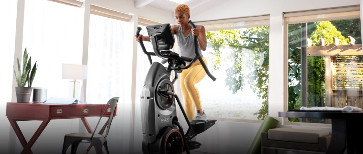 A woman exercising on a Max Trainer compact elliptical from her home office.