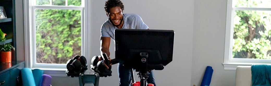 Man riding a bowflex bike in his home with other workout equipment in the background